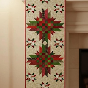May include: A rectangular Christmas table runner. The runner has a cream background with small star patterns. Two large starburst designs in red and green are in the centre, with smaller stars between them. The edges are trimmed in red.