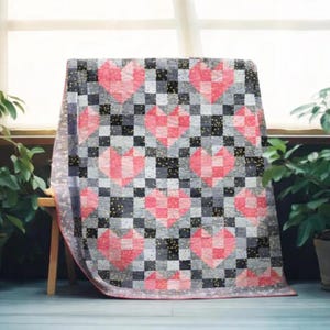 Peut inclure: Une courtepointe faite à la main avec un motif répété de cœurs roses sur un damier de carrés gris, noirs et blancs. La courtepointe a une bordure rose et est drapée sur un banc en bois. La courtepointe mesure environ 152 cm sur 178 cm.