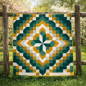 May include: A geometric quilt with a starburst design, displayed outdoors. The quilt features a pattern of teal, gold, white, and gray squares. The quilt is hanging on a wooden fence, with a background of green grass and flowering trees.
