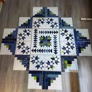 May include: A collection of quilt blocks arranged on a wooden floor. The blocks feature various geometric patterns in shades of blue, white, and green. Some blocks have star designs, while others have a log cabin style.