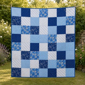 Pode incluir: Uma colcha de retalhos composta por uma grade de painéis de tecido quadrados em vários tons de azul e branco. Os padrões incluem bolinhas, listras diagonais, xadrez vichy e estampas florais, unidos por uma borda azul sólida.