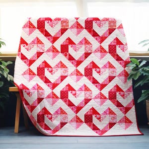 May include: A red and white quilt with a repeating heart pattern. The quilt features various shades of red and pink hearts against a white background. The quilt is draped over a wooden bench, showcasing its design.