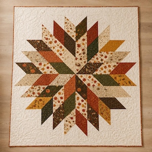 Könnte beinhalten: Ein quadratischer Quilt mit einem zentralen Sternmuster aus rautenförmigen Stoffstücken in Orange-, Dunkelgrün-, Braun- und Cremetönen. Die Stoffstücke zeigen herbstliche Drucke von Blättern und Kürbissen auf einem cremefarbenen Hintergrund.