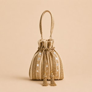 May include: A gold-toned drawstring handbag featuring vertical embroidered stripes, small reflective mirror accents, and a single top handle. The bag is cinched with a braided cord that ends in two decorative tassels, creating a structured pouch shape.