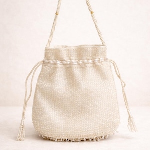 Può includere: Borsa a coulisse con perline color avorio con manico intrecciato e dettagli color oro. La borsa presenta una superficie strutturata e una delicata frangia lungo il bordo inferiore. Un piccolo accessorio elegante per occasioni speciali.