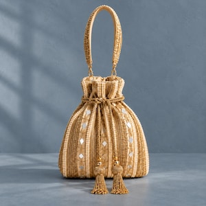 May include: A gold and beige drawstring handbag featuring intricate embroidery, vertical beaded stripes, and small diamond-shaped mirror accents. The bag includes a single beaded top handle and two long, dangling gold tassels at the front closure.