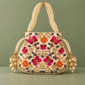 May include: A cream-colored handbag featuring intricate floral embroidery in shades of hot pink, orange, and slate blue. The bag is accented with gold-toned beadwork and features a handle and side tassels constructed from strands of white pearls.