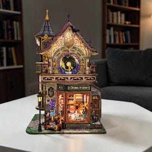 May include: A detailed wooden model of a whimsical shop, "Chronos Arcanum," with a clock tower and illuminated interior. The shop features a sign, a street lamp, and decorative elements. The color scheme includes purple, gold, and brown.