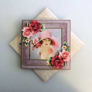 May include: A framed vintage image of a woman wearing a pink hat, surrounded by red and pink roses. The frame is a soft purple color, and the image is set on a patterned background. The overall theme is vintage and floral.