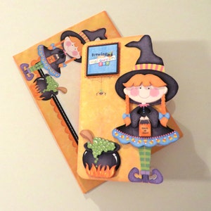 May include: A Halloween card with a witch holding a trick or treat bag. The card is decorated with a cauldron, a spider web, and the text "Brewing Halloween Fun".
