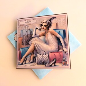 May include: A greeting card featuring a woman in a white dress sitting amidst shopping bags. The card has the text "Just for You" on the front.