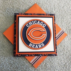 May include: A handmade greeting card featuring the Chicago Bears logo. The card is made with layers of orange, blue, and white cardstock and features a 3D effect. The logo is a circle with the words "Chicago Bears" and a stylized "C" in the center.