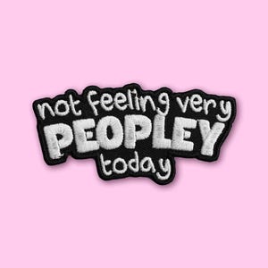 Può includere: Una toppa ricamata nera con testo bianco cucito che recita not feeling very PEOPLEY today. La toppa ha un bordo nero spesso e una forma arrotondata e irregolare che segue il contorno delle lettere in un carattere grassetto senza grazie.