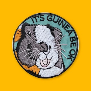 May include: A round, green and white embroidered patch with a guinea pig face and the text "It's Guinea Be Ok".