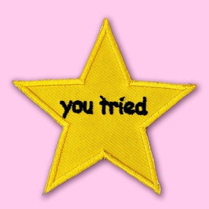 以下が含まれることがあります： 黒い刺繍で「you tried」と書かれた黄色の星形のワッペンです。