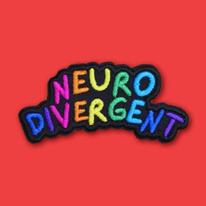 Pode incluir: Um remendo bordado com cores do arco-íris com as palavras "Neuro Divergent" em um contorno preto.