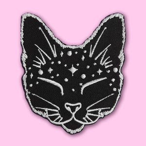 Könnte beinhalten: Schwarzer gestickter Bügel-Patch mit einem Katzenkopf und weißen sternförmigen Details.