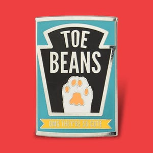 May include: A rectangular enamel pin with a teal border and a red background. The pin features the words "TOE BEANS" in white, a paw print, and the text "OMG THEY'RE SO CUTE" in yellow.