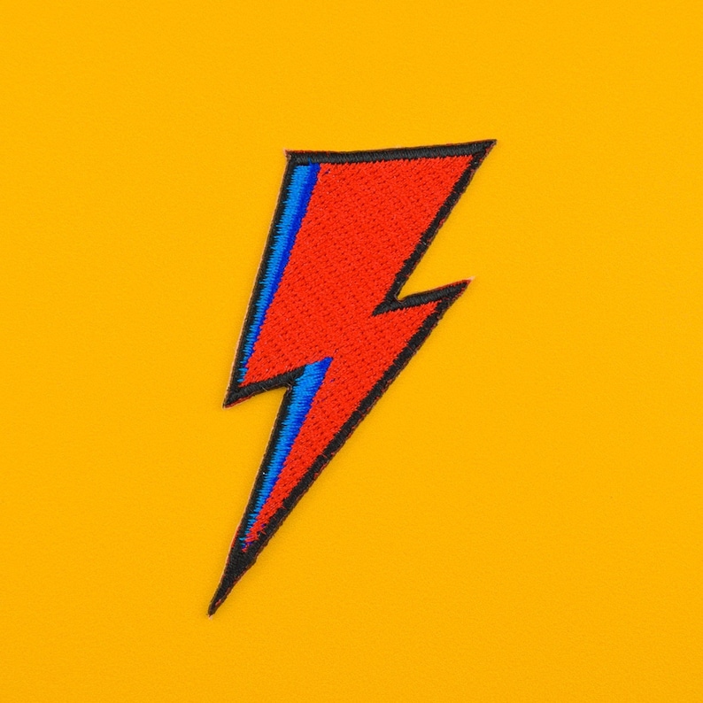 Peut inclure: Un patch en forme d'&eacute;clair rouge et bleu avec des coutures noires. Le patch est sur un fond jaune.