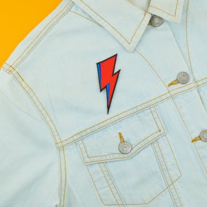 Peut inclure: Une veste en jean bleu clair avec un patch en forme d'&eacute;clair rouge et bleu sur le devant. Le patch est cousu sur le c&ocirc;t&eacute; gauche de la veste, juste en dessous du col.