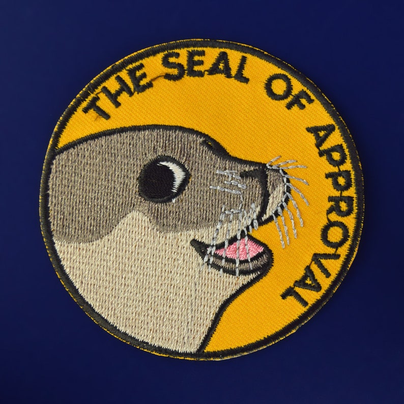 May include: A yellow embroidered patch with a cartoon seal and the text "The Seal of Approval".