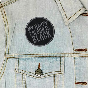 May include: A black and grey embroidered patch with the text "My Happy Colour Is Black" on a light blue denim jacket.