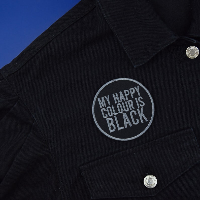 May include: Black denim jacket with a grey embroidered patch that says "My Happy Colour Is Black".