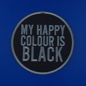 May include: A black and grey circular patch with the text "My happy colour is black" embroidered in grey.