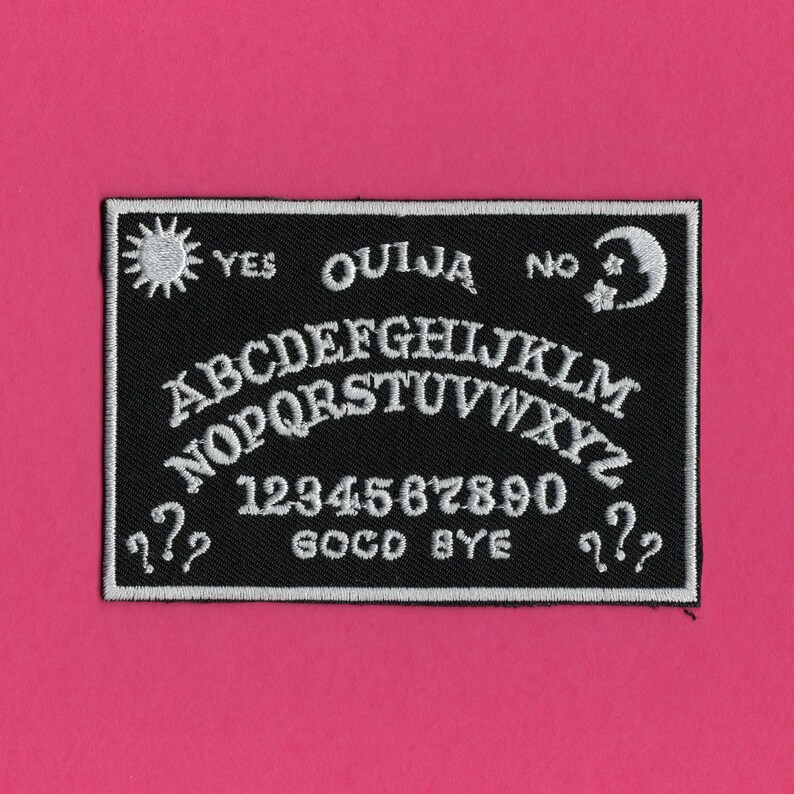 May include: Black and white embroidered patch with a Ouija board design. The patch features the letters of the alphabet, numbers 1-9 and 0, the words "Yes", "No", "Goodbye", and symbols of a sun and a crescent moon.