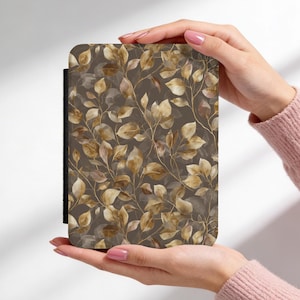 May include: A rectangular case featuring a repeating pattern of stylized leaves in shades of brown and gold against a dark brown background. The case has a black spine and is held by two hands.