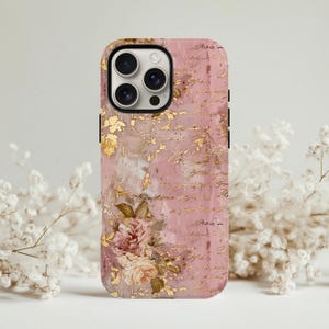 Könnte beinhalten: Eine rosa Handyhülle mit floralem Design und Goldblatt-Akzenten. Die Hülle zeigt eine Ansammlung von rosa und cremefarbenen Rosen und schriftartigem Text. Die Hülle hat einen schwarzen Rand und einen Kameraausschnitt.