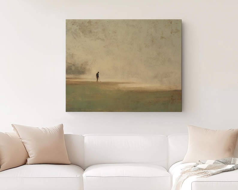 May include: Square canvas art print depicting a solitary figure on a golf course. The artwork features a muted color palette of greens, browns, and beige, creating a serene and contemplative atmosphere. The print is displayed above a white sofa.