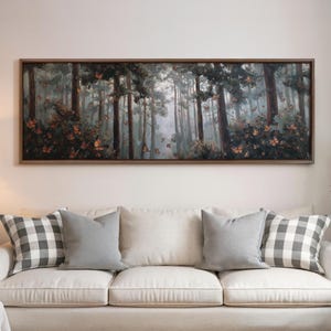 May include: A framed landscape painting depicts a forest scene with tall trees and butterflies. The artwork is in a dark wooden frame and hangs above a cream-colored sofa with gray and plaid pillows.