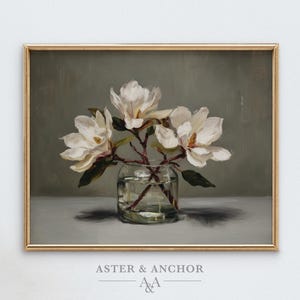 May include: A framed painting of white magnolia flowers in a clear glass vase. The artwork has a gold frame and features a muted color palette with a focus on the flowers and their delicate petals. The text "ASTER & ANCHOR" is at the bottom.
