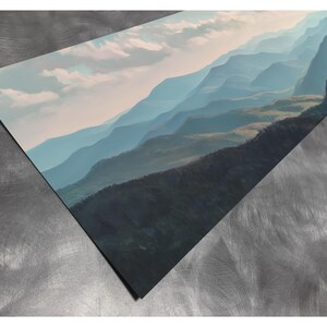 May include: A print of a mountain landscape in shades of blue and green, with a cloudy sky. The artwork depicts rolling hills and distant peaks, creating a sense of depth and tranquility. The print is displayed at an angle.