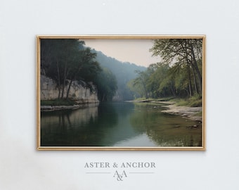 May include: A framed print of a tranquil river landscape. The artwork shows a calm river reflecting the surrounding green trees and rocky cliffs. The print is in a gold frame, with the text "ASTER & ANCHOR" at the bottom.