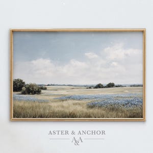 May include: A framed landscape painting depicts a serene field of wildflowers under a cloudy blue sky. The artwork features a gold-colored frame and the text "ASTER & ANCHOR" at the bottom.