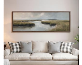 May include: A landscape painting in a dark wooden frame shows a marsh scene with a river. The artwork hangs above a cream sofa with grey cushions. The painting's dimensions are not specified.