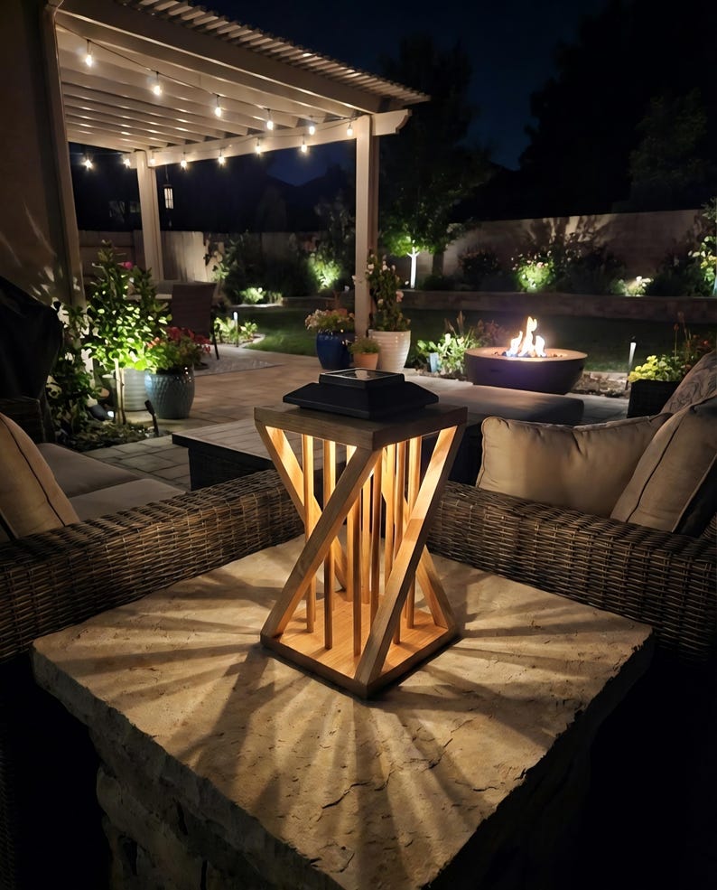 Peut inclure: Une lanterne d'ext&eacute;rieur en bois au design g&eacute;om&eacute;trique est pos&eacute;e sur une table en pierre. La lumi&egrave;re de la lanterne projette un motif en &eacute;toile sur la surface de la table. L'arri&egrave;re-plan pr&eacute;sente un cadre de patio avec un foyer et des guirlandes lumineuses.