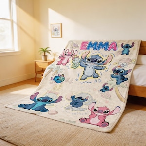 May include: A beige throw blanket featuring multiple cartoon images of Stitch and Angel. The blanket has the name "EMMA" in pink and blue letters. The blanket is on a bed in a well-lit room.