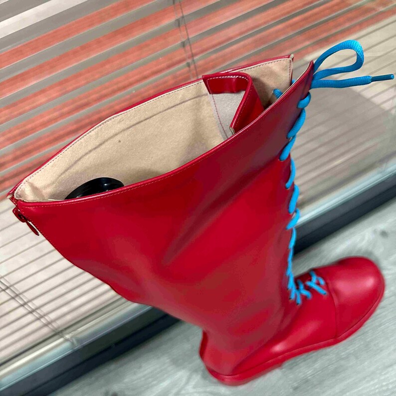 May include: A tall, red boot with bright blue laces. The boot has a smooth, glossy finish and a round toe. The laces are threaded through eyelets up the front of the boot. The interior of the boot is a light beige color.