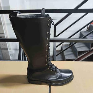 Puede incluir: Una bota alta de color negro con acabado liso, punta redondeada y cierre frontal de cordones con ojales met&aacute;licos plateados. La bota incluye una cremallera vertical a lo largo de la parte trasera de la ca&ntilde;a y una suela de goma negra resistente.