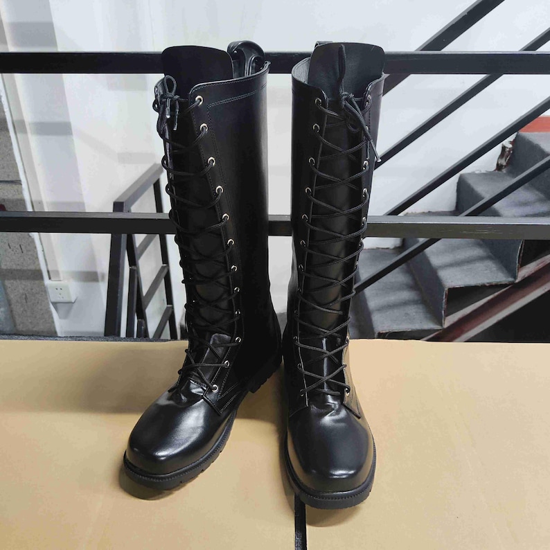 Puede incluir: Un par de botas negras hasta la rodilla con acabado liso, punteras redondeadas y cierre frontal completo de cordones con ojales met&aacute;licos plateados. Las botas cuentan con una suela negra plana y resistente.