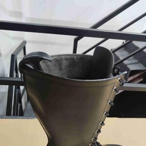 Puede incluir: Una bota alta de color negro con un acabado exterior liso, un forro interior gris oscuro y una fila vertical de ojales met&aacute;licos de color plateado en el lateral. Un calzador de pl&aacute;stico negro est&aacute; insertado en la abertura superior.