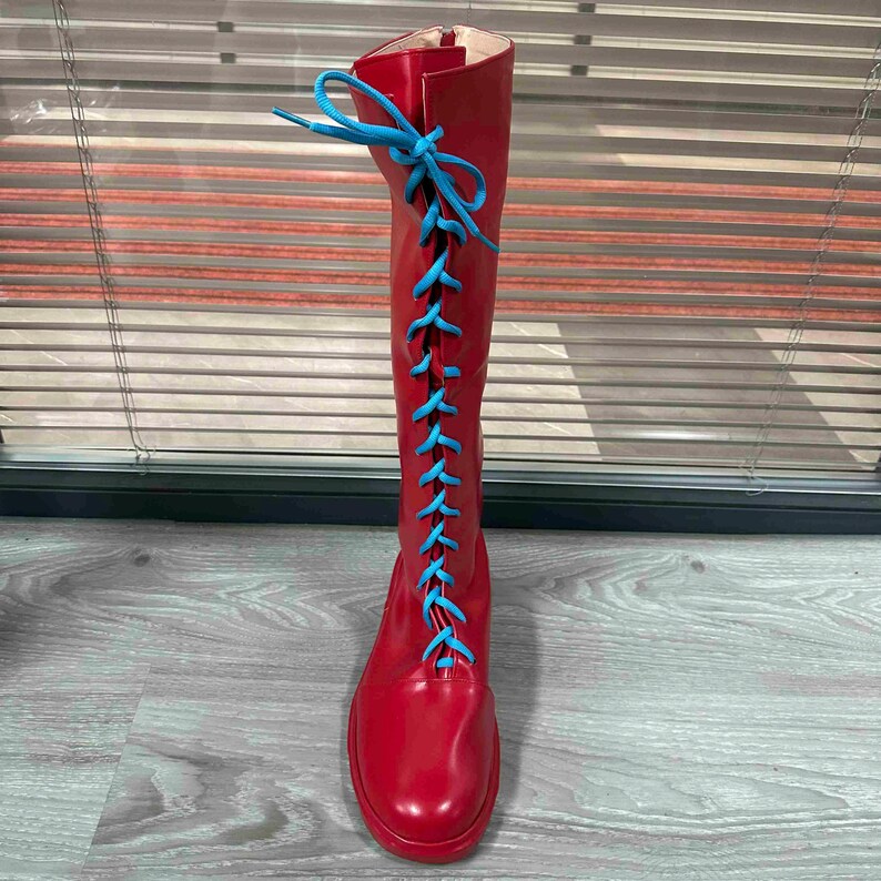 May include: A tall, red boot with bright blue laces. The boot is made of a shiny material and has a round toe. The laces run up the front of the boot, creating a striking contrast against the red. The boot is knee-high.