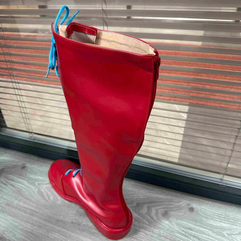 May include: A tall, red boot with a glossy finish. The boot features a round toe, a zipper on the side, and light blue laces. The boot is knee-high and appears to be made of a smooth, synthetic material.