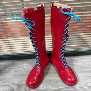 May include: A pair of knee-high red boots with light blue laces. The boots have a glossy finish and a round toe. The laces are tied in a bow at the top of the boot.