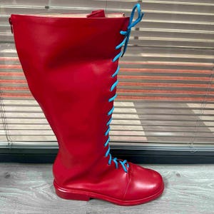 May include: A tall, red boot with a rounded toe and a knee-high shaft. The boot features light blue laces that run up the front and tie at the top. The boot is made of a smooth material and has a zipper on the back.