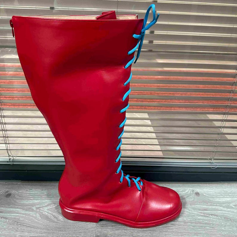 May include: A tall, red boot with a rounded toe and a knee-high shaft. The boot features light blue laces that run up the front and tie at the top. The boot is made of a smooth material and has a zipper on the back.