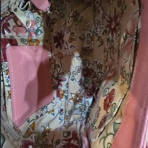 Peut inclure: Sac &agrave; main en cuir rose avec un int&eacute;rieur &agrave; motifs floraux. Le sac est dot&eacute; d'une &eacute;tiquette en cuir rose et d'une fermeture &eacute;clair argent&eacute;e. La doublure int&eacute;rieure est de couleur cr&egrave;me avec un motif de fleurs et de papillons.